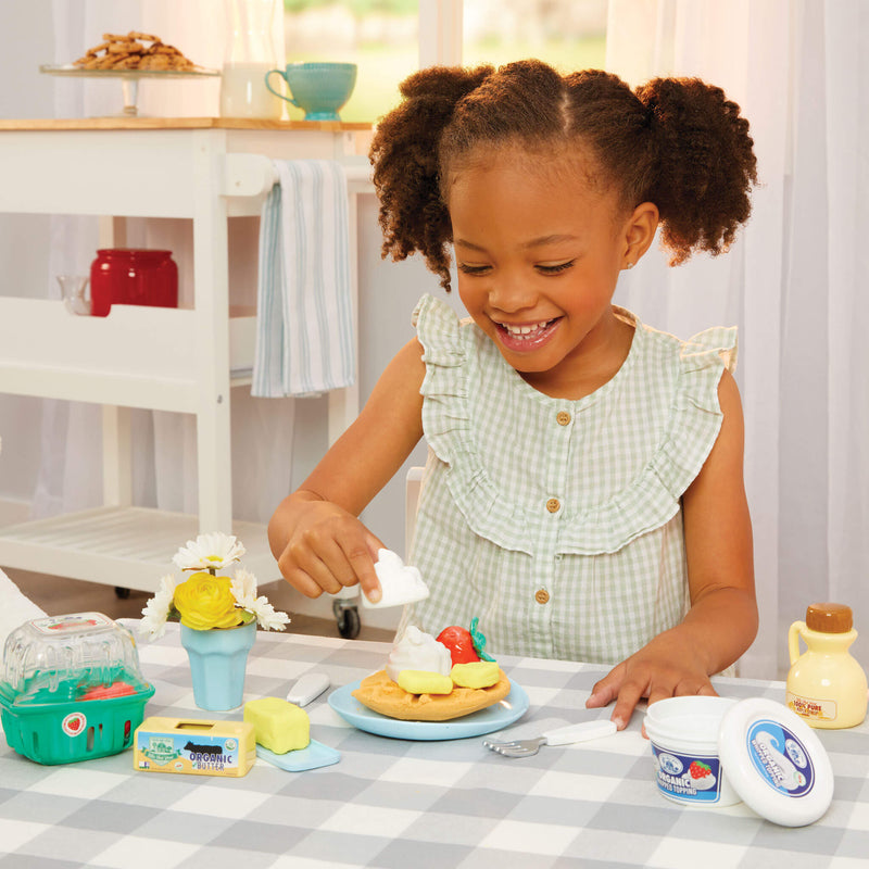 girl adding butter and whip cream to top of waffle